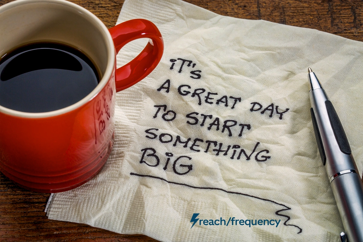 Coffee cup next to a napkin with handwritten note 'It's a great day to start something BIG' and a pen, illustrating the first step in setting marketing goals